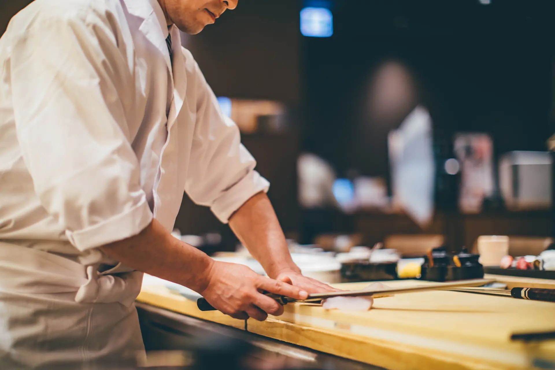 寿司職人がカウンターで包丁を握り、魚をさばいている所作